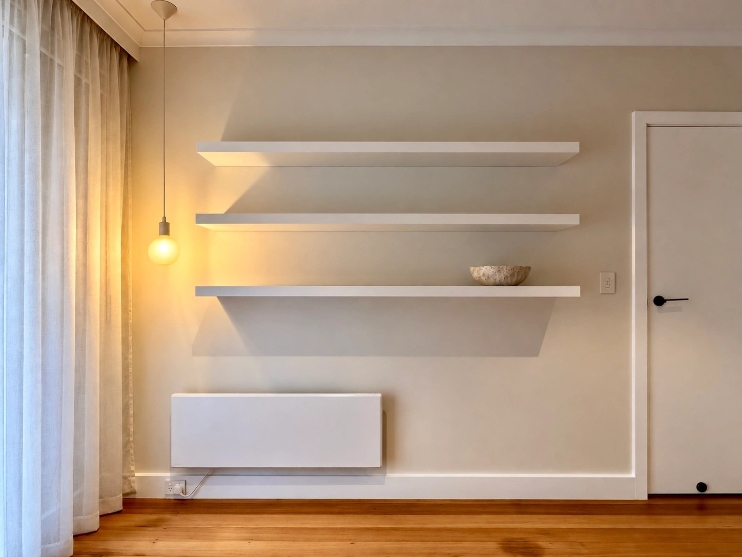 White floating shelves on a cream wall above timber floors